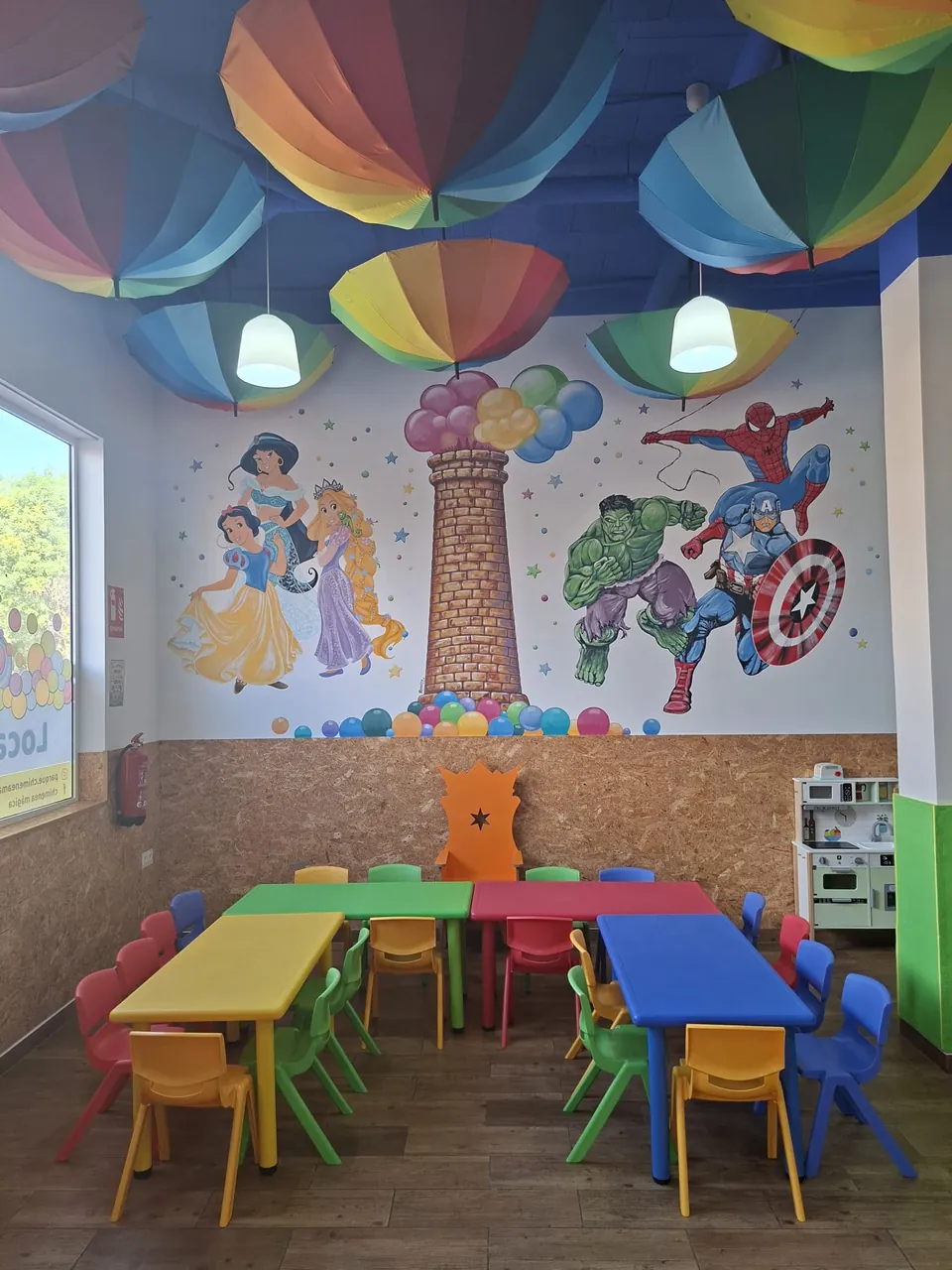 El salón: mesas de colores, la silla de la corona y el mural de nuestra chimenea bajo los paraguas